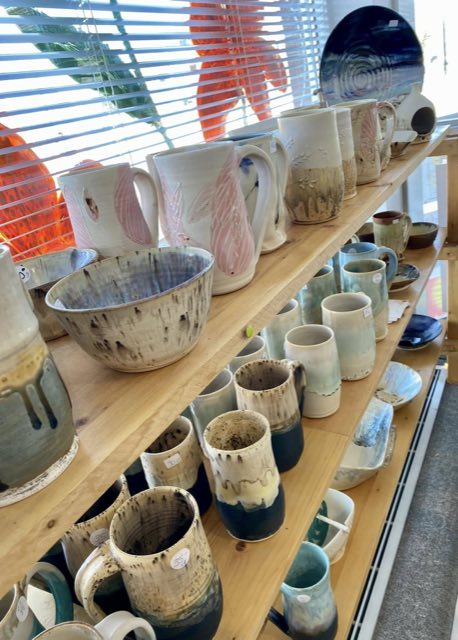 Shelves of handmade pottery mugs and bowls at On the Avenue Gallery
